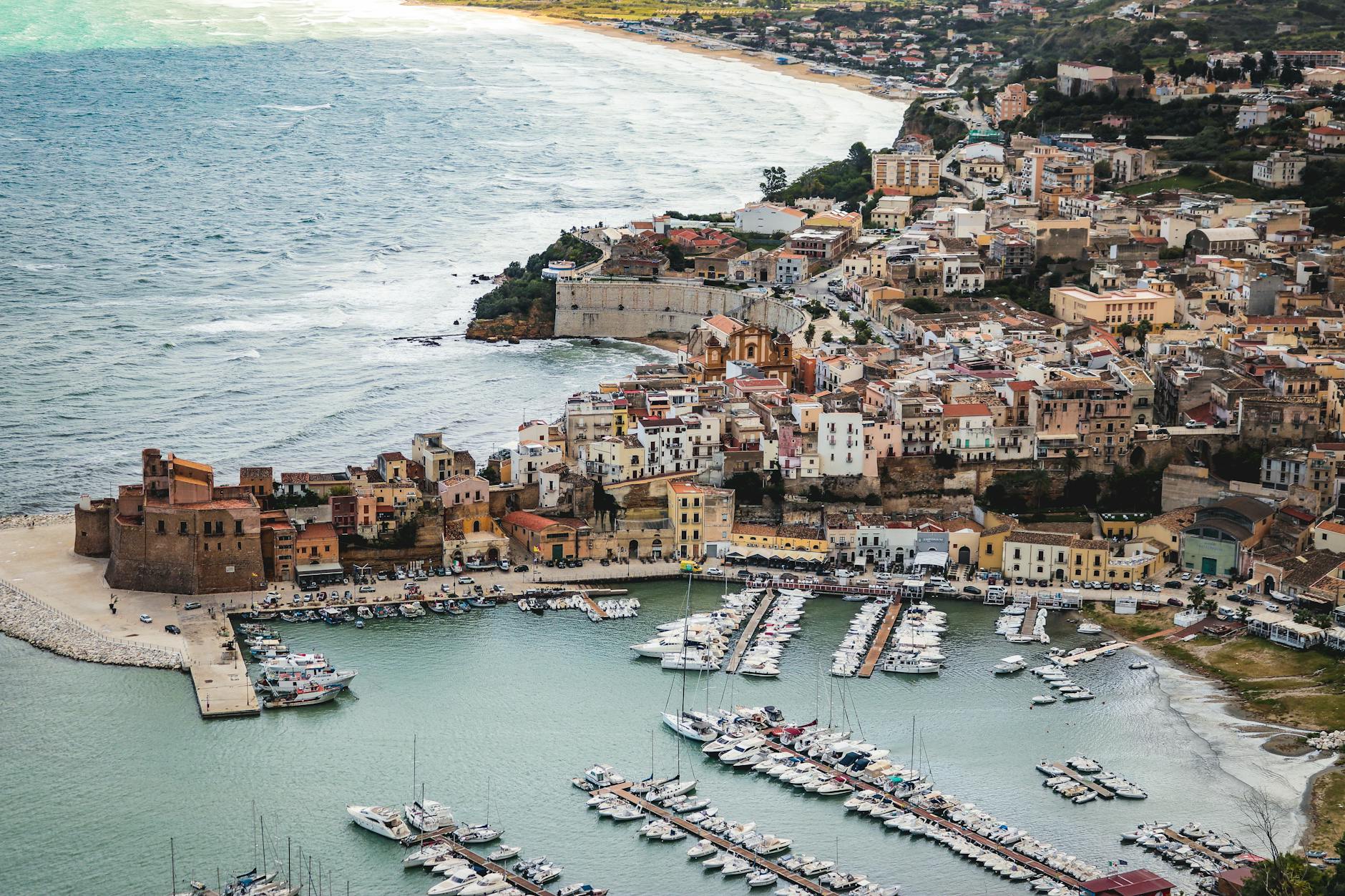 Aerial view of Sicilian coastal town with marina and historic architecture overlooking the Mediterranean