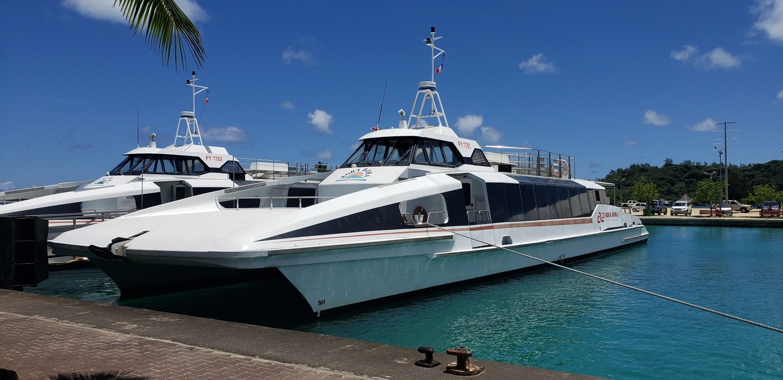 A white passenger catamaran ferry tied up at a dock beside a second boat, under a blue sky in Bora Bora.