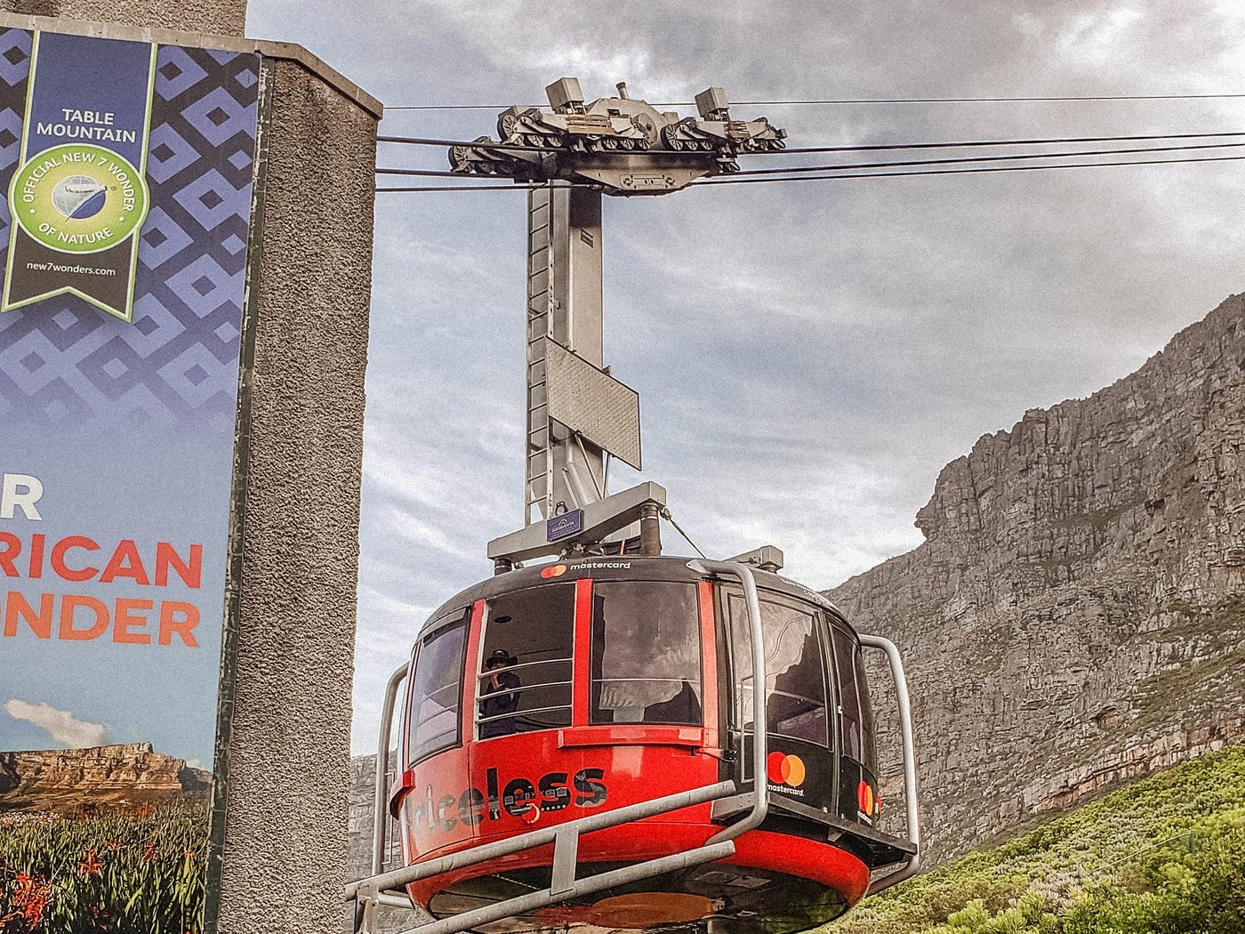 A red Table Mountain cable car cabin hanging below the cableway with cliffs behind it.