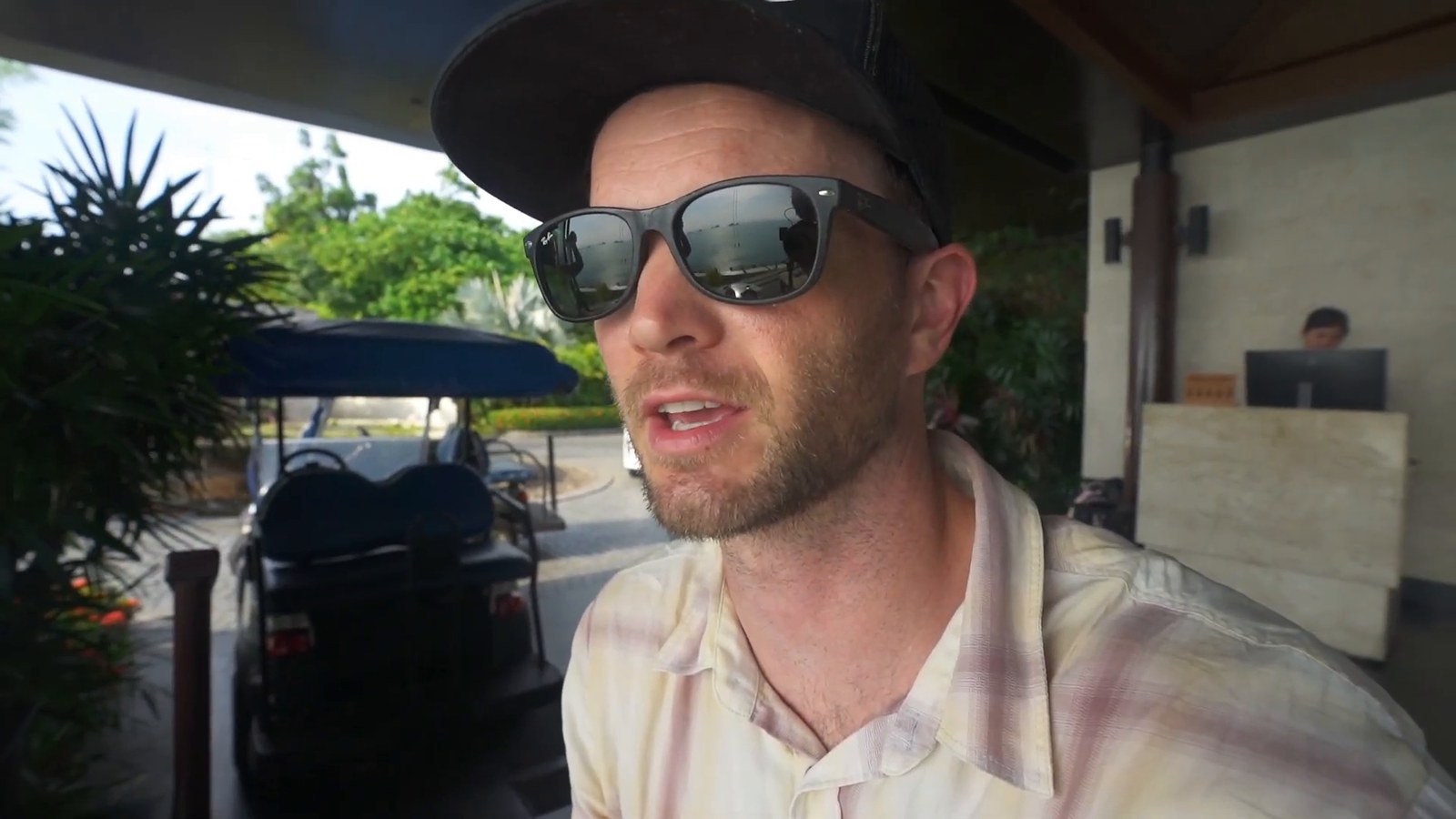 A man in sunglasses and a cap at the resort's arrival lobby, with a resort golf buggy parked behind him.