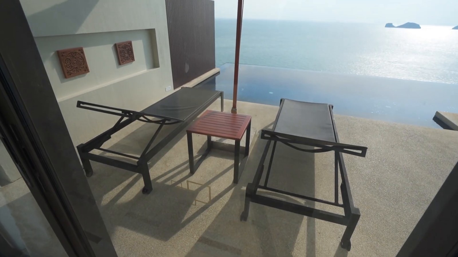A private infinity pool and deck with two loungers and an umbrella, looking out over the sea to a distant island.