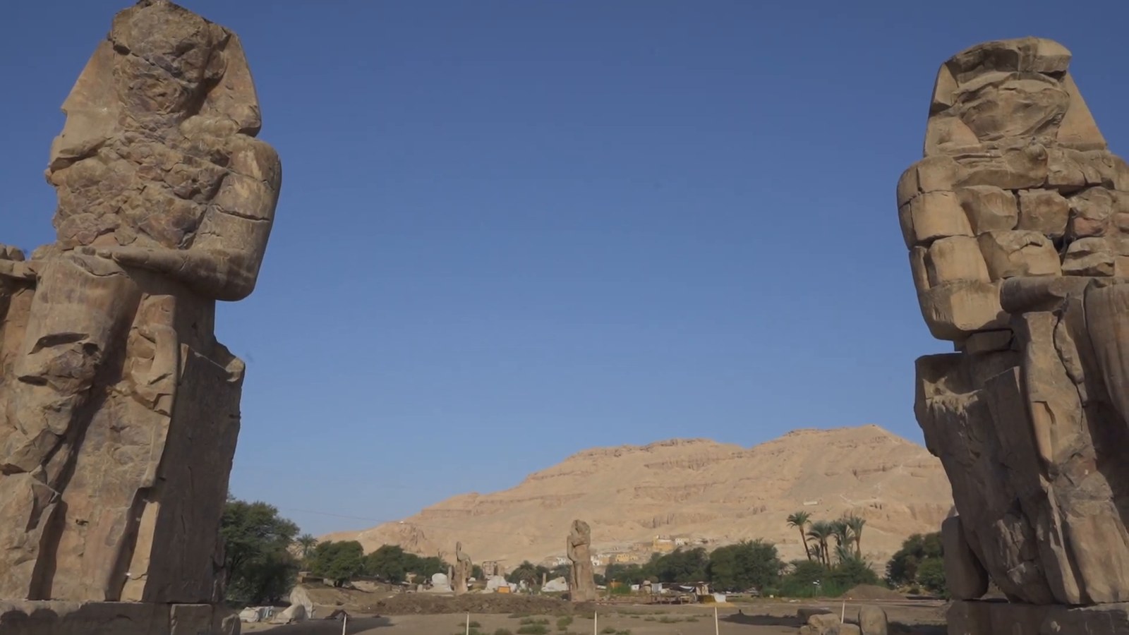 Two weathered giant seated statues framing a view of desert cliffs on Luxor's West Bank.