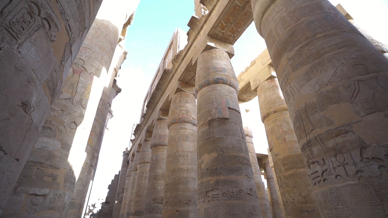 Looking up at massive carved columns in the hall of pillars at Karnak Temple, with hieroglyphs and traces of colour.