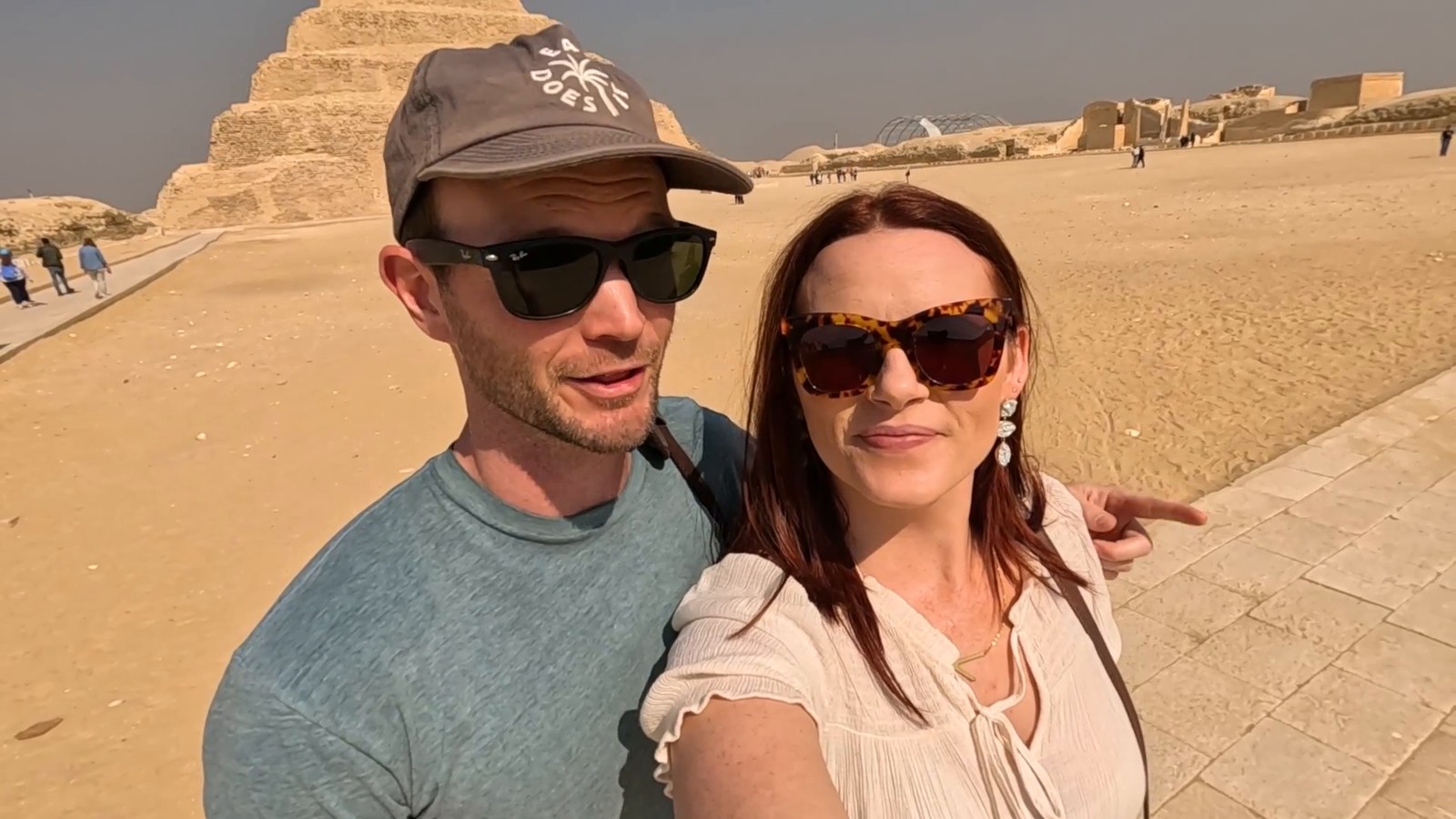A man in a cap and a woman in sunglasses taking a selfie in front of the Step Pyramid of Djoser at Saqqara.