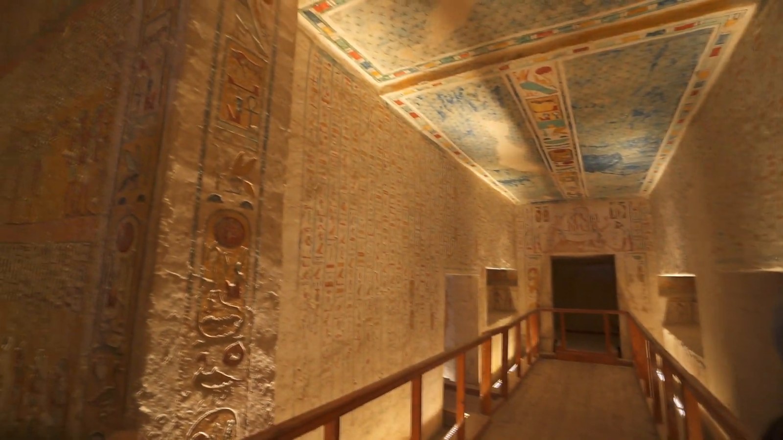 A long tomb corridor in the Valley of the Kings with a painted ceiling, carved walls and a wooden walkway.