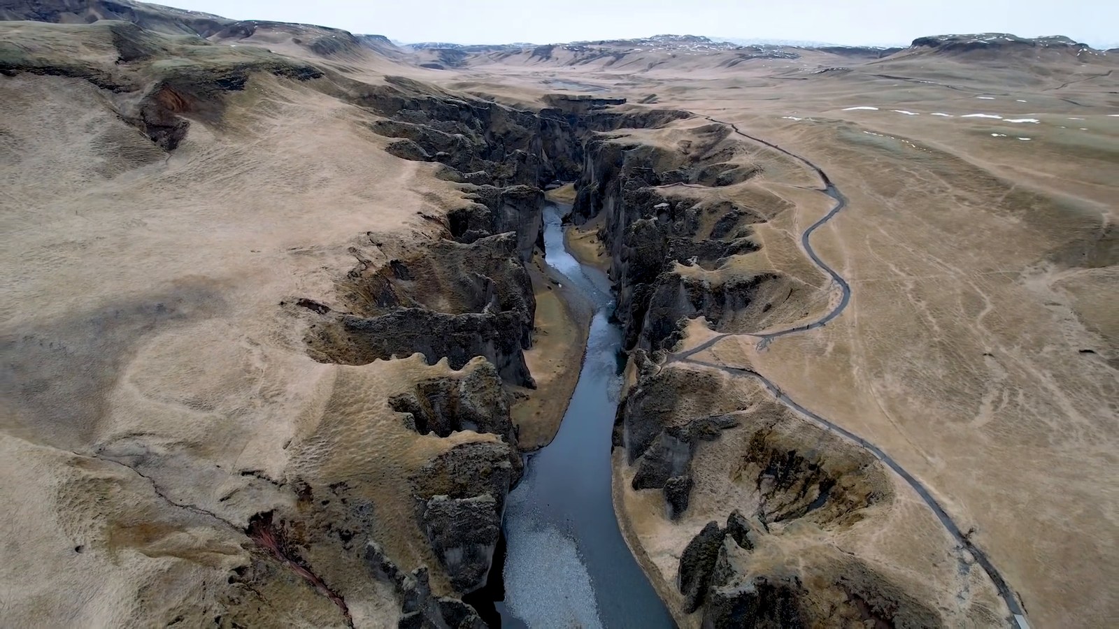 Aerial view of a deep winding canyon with a river at the bottom and a path along the rim.