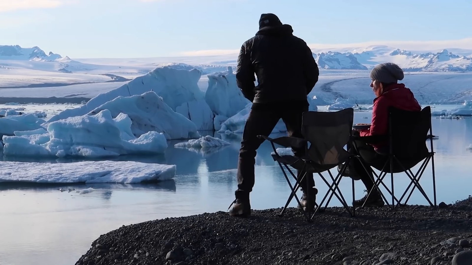 Two people in camp chairs at the edge of Jökulsárlón glacier lagoon with icebergs and glacier behind them.