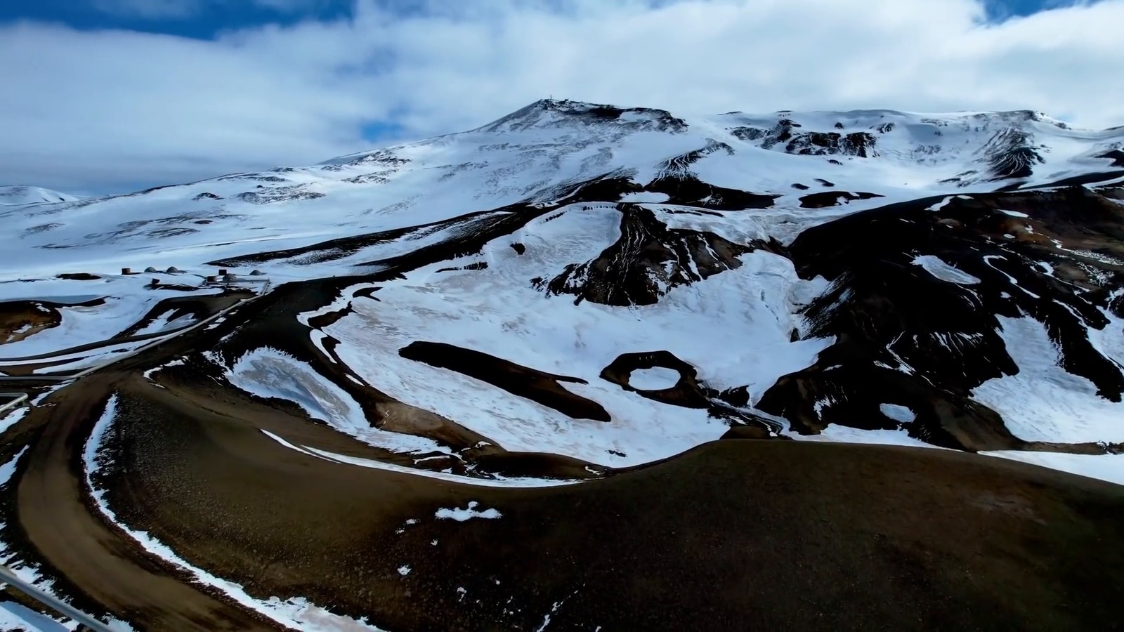 Aerial view of a snow-covered volcanic landscape with brown ridges and a road below.