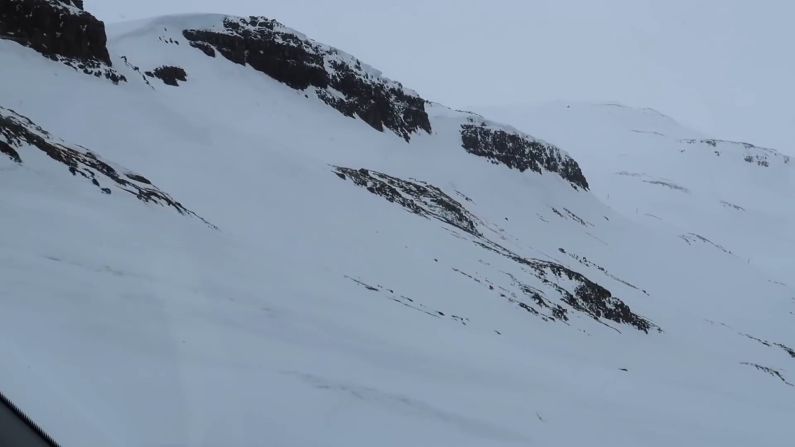 A snow-covered mountainside with bands of dark rock under a grey sky.