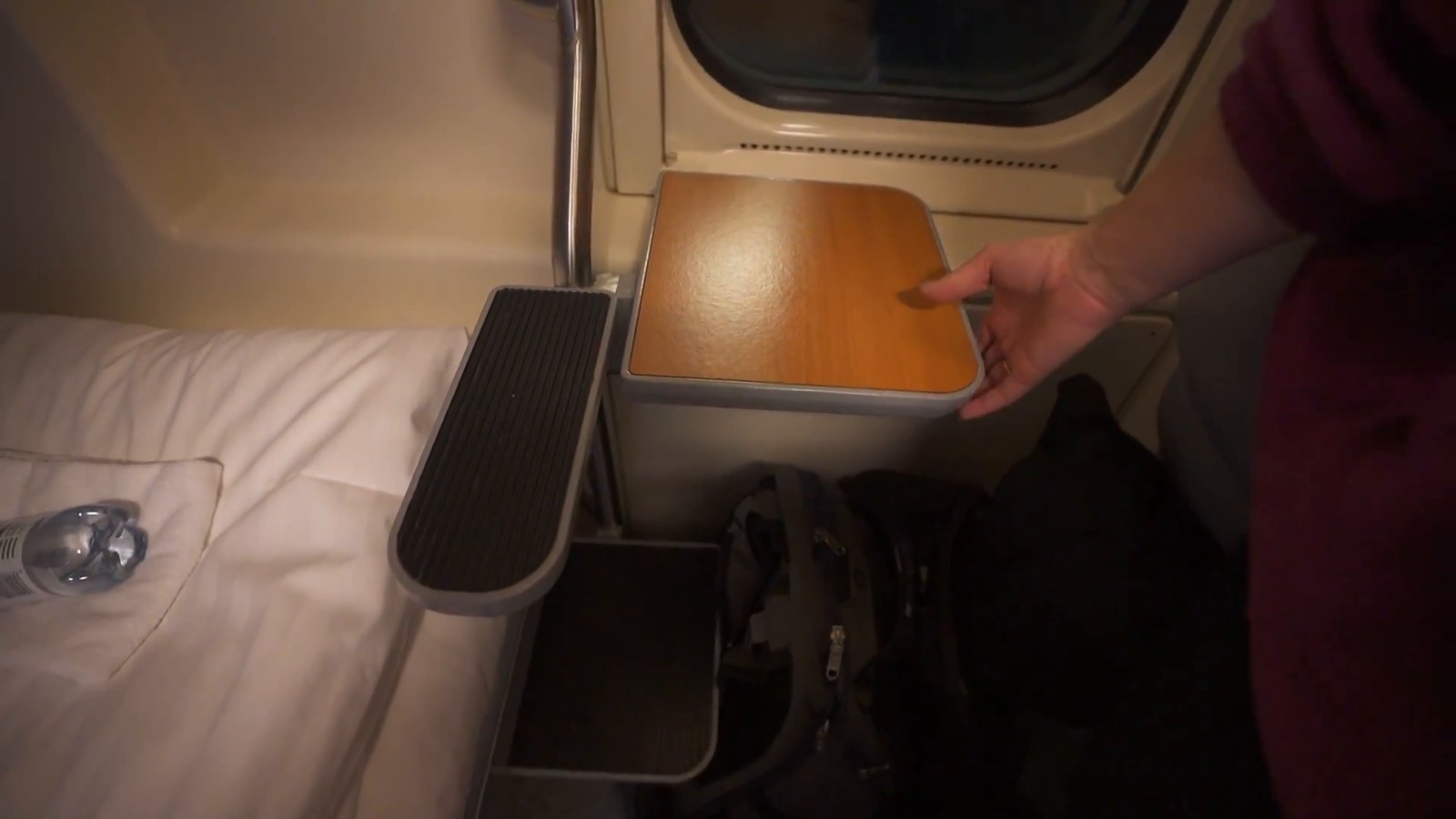 A close view of a small fold-down wooden desk and ladder rung beside a made-up train bunk bed.