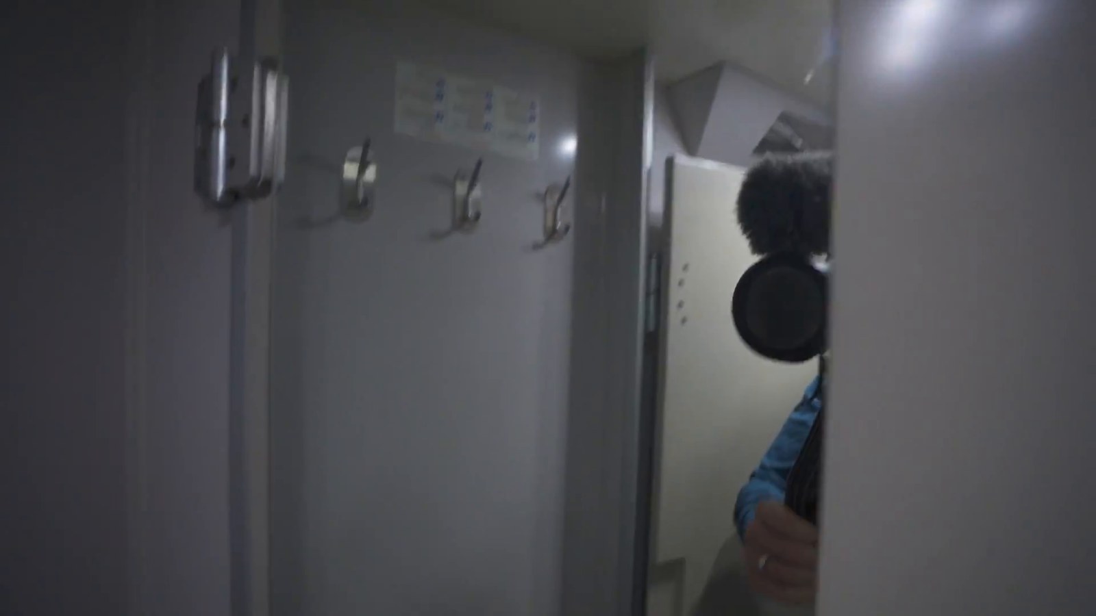 A narrow train corridor area with coat hooks on a door, showing the changing area outside the shared shower.