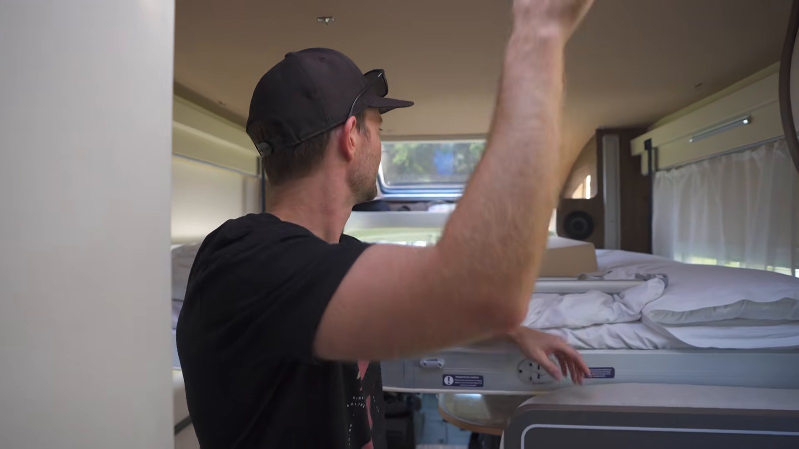 A man pulling down a made-up double bed from the ceiling of a motorhome above the seating area.