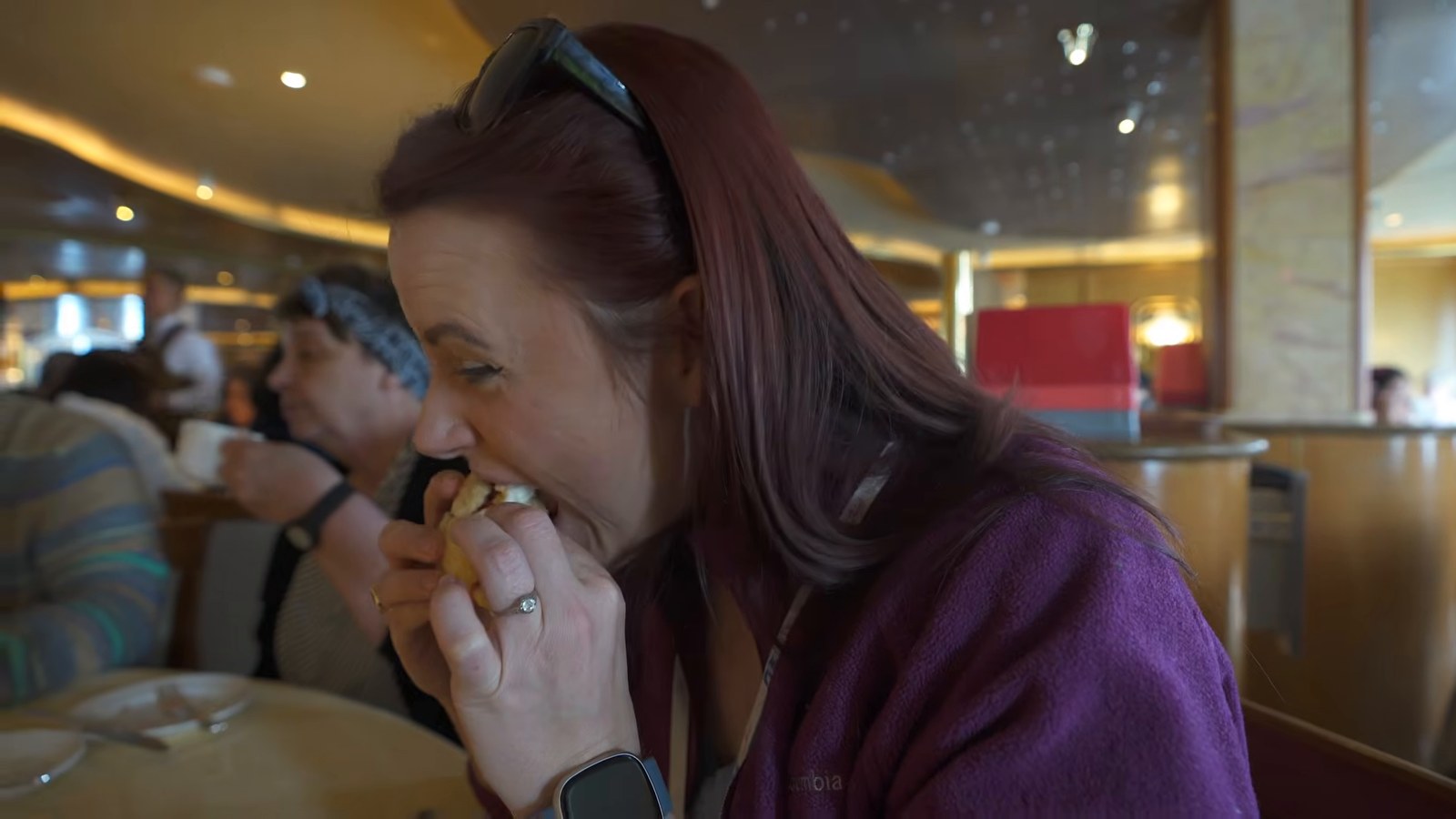 A man and a woman seated at a table inside a cruise ship dining room, eating pastries.