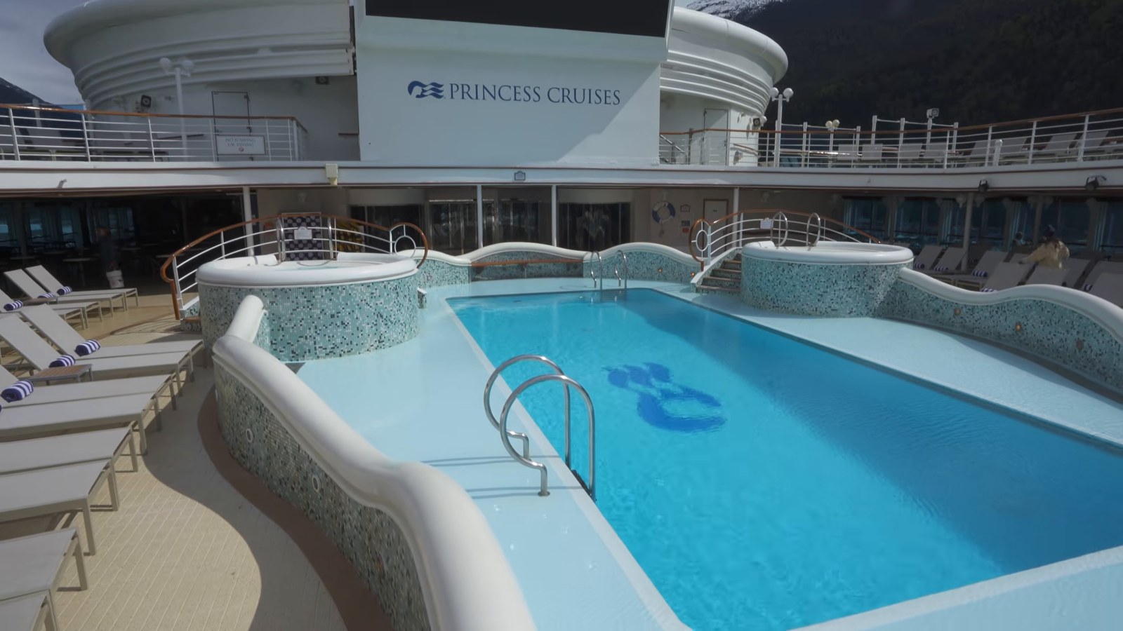 An empty outdoor pool with a Princess Cruises logo tiled into the bottom, mountains visible in the distance.