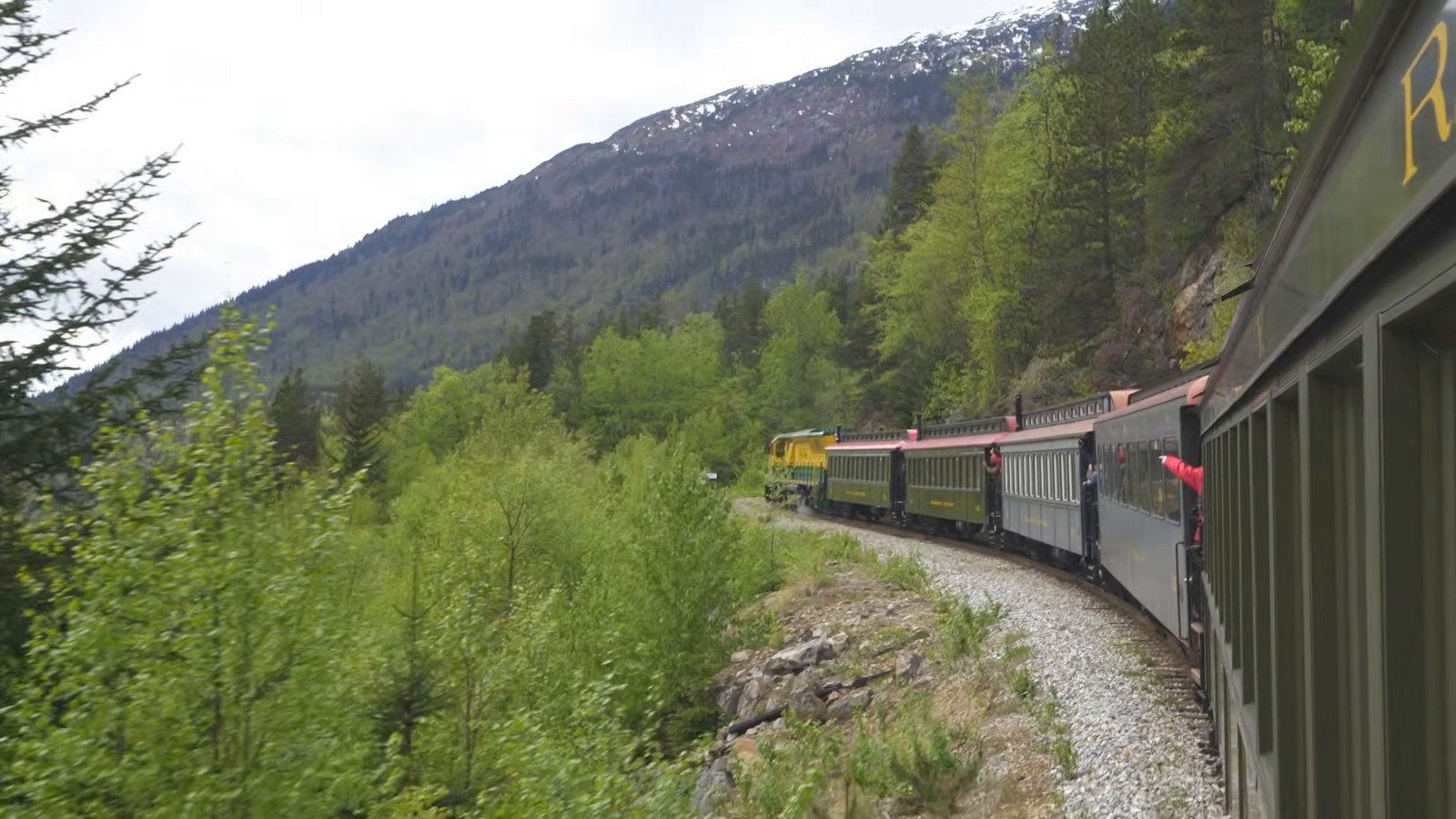 A narrow-gauge train curving along a forested hillside track, seen from one of its cars.