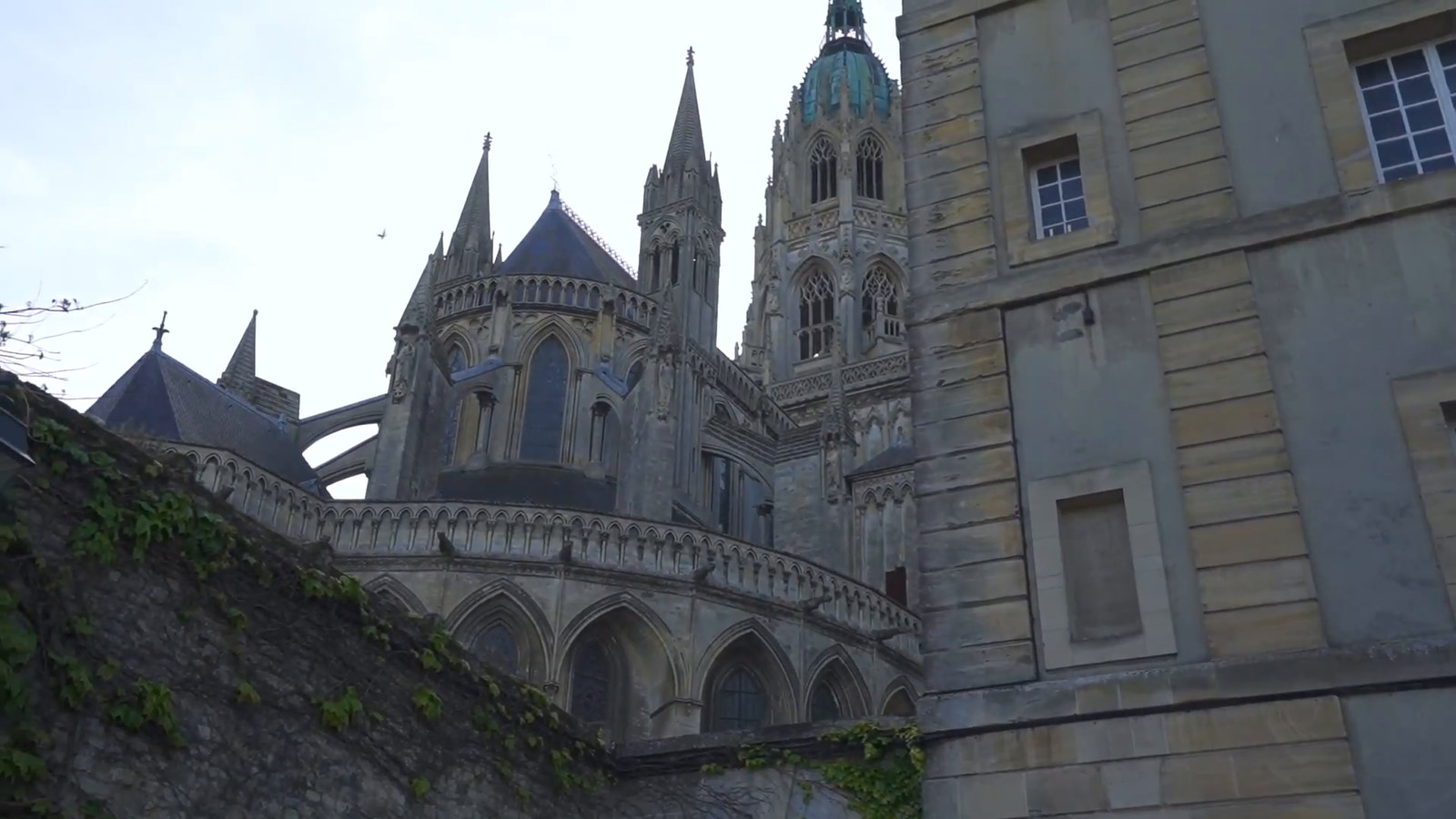 The Gothic spires and flying buttresses of Bayeux Cathedral seen from a quiet side street.