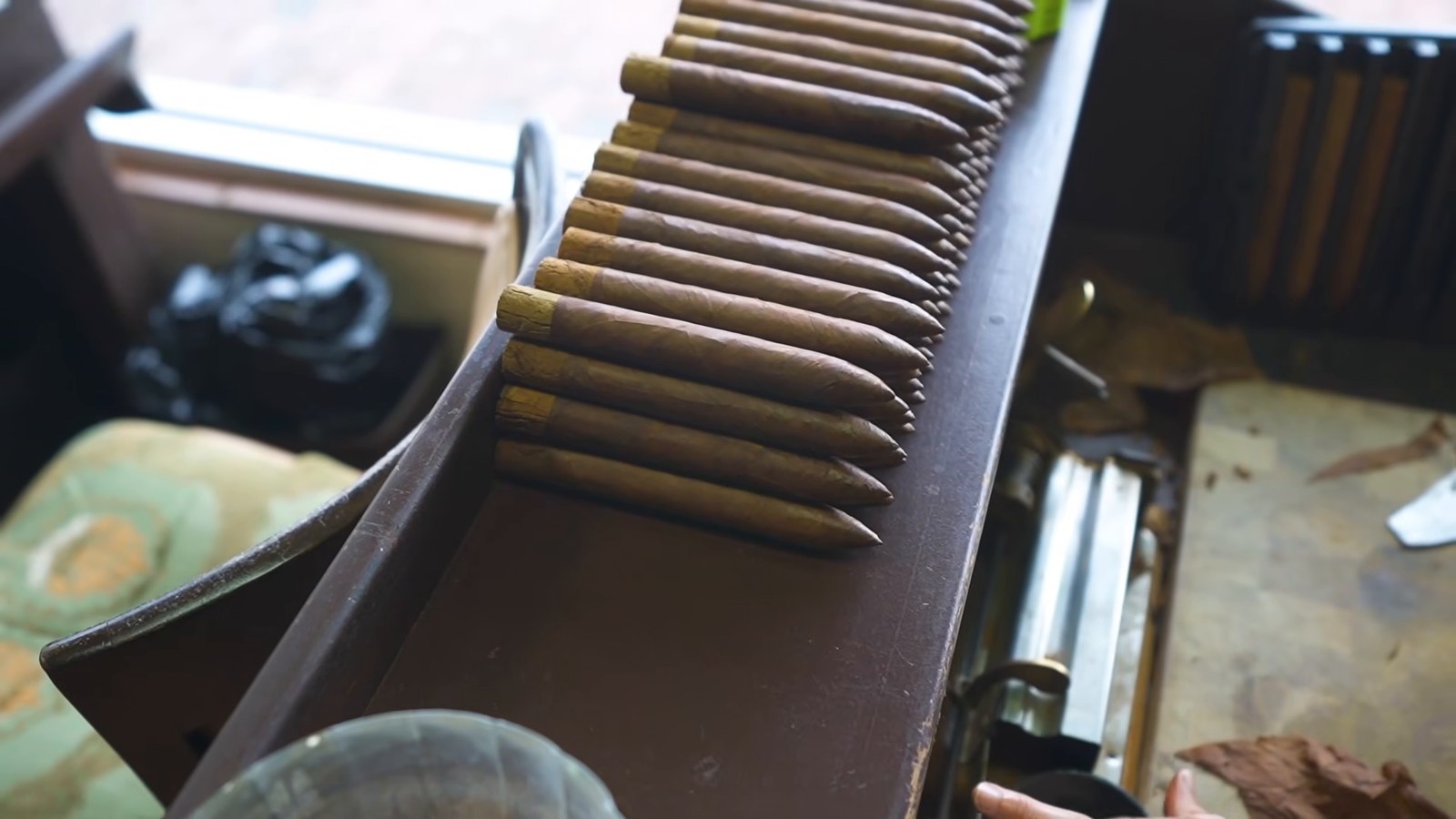 Rows of rolled cigars lined up on a dark wooden tray at a cigar shop.