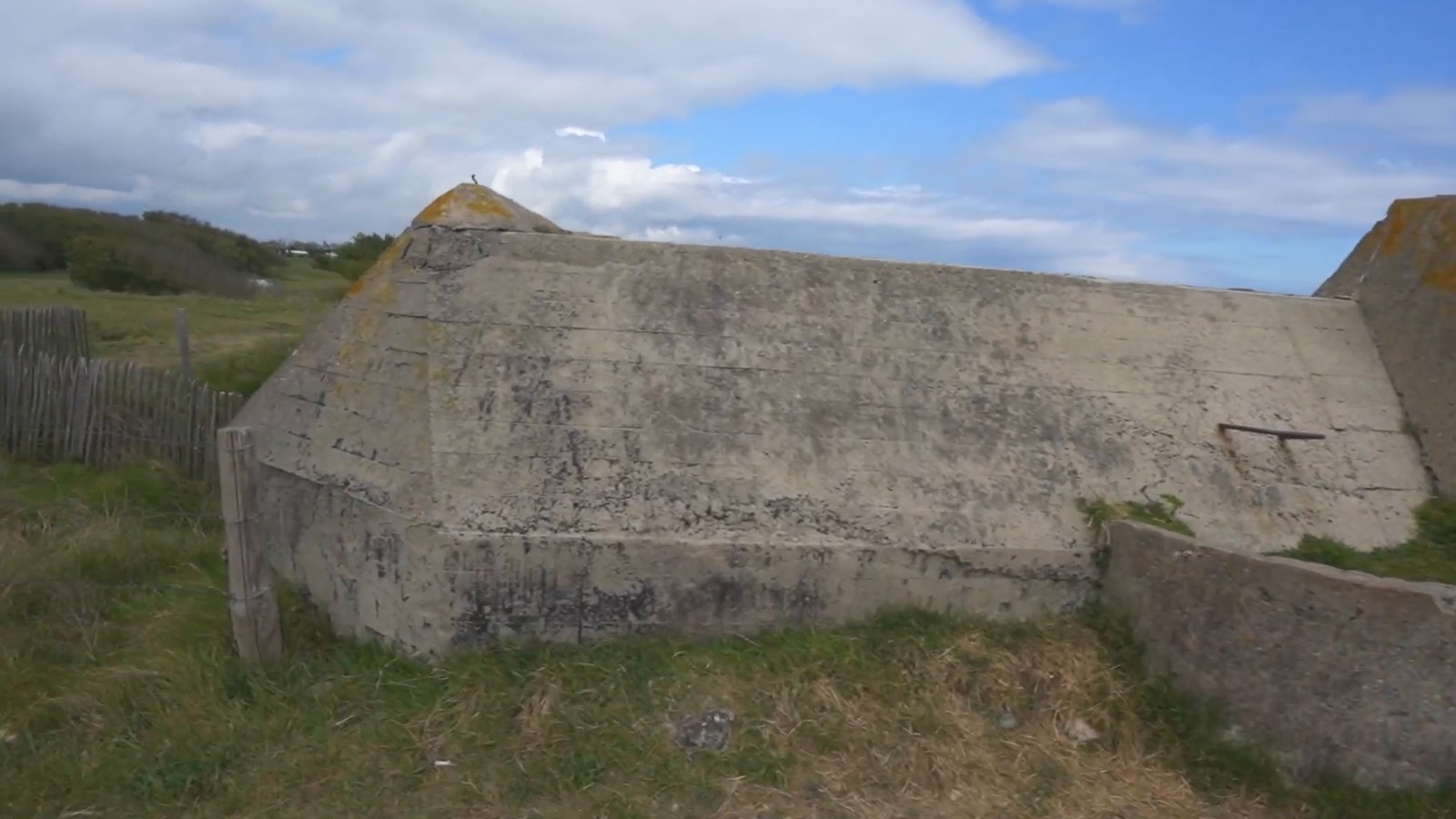 A weathered concrete bunker sits low in a grassy field under a partly cloudy sky.