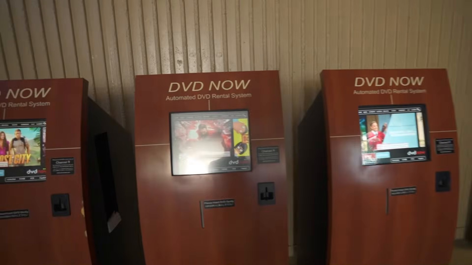Three automated DVD rental kiosks standing against a wood-panelled wall.