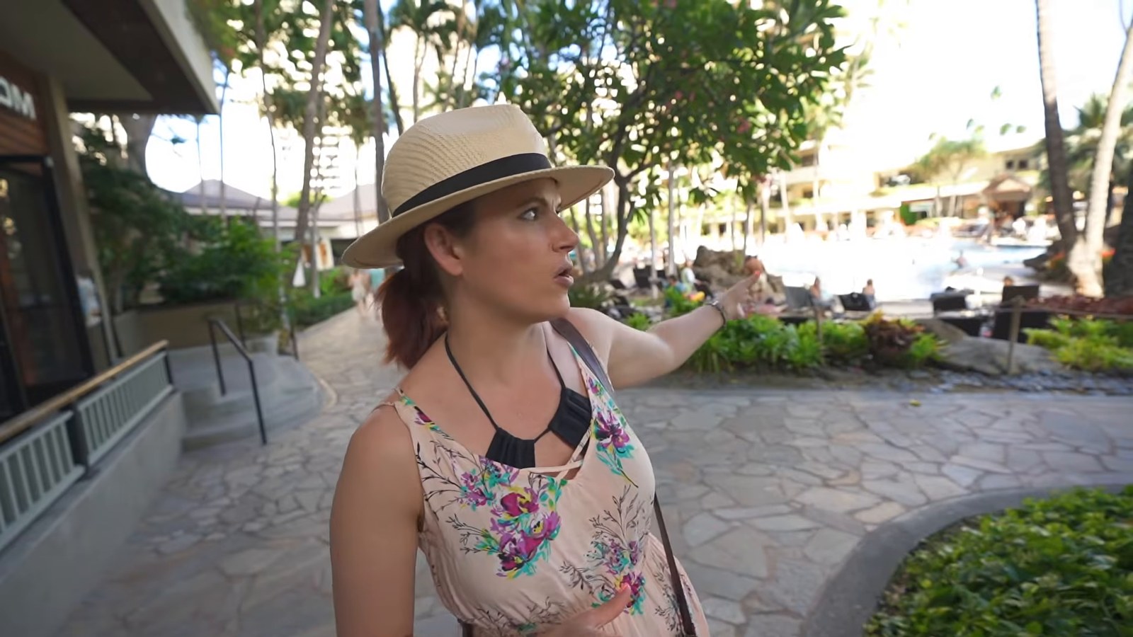 A woman in a straw hat points along a stone-paved walkway toward the pool area of Hilton Hawaiian Village.