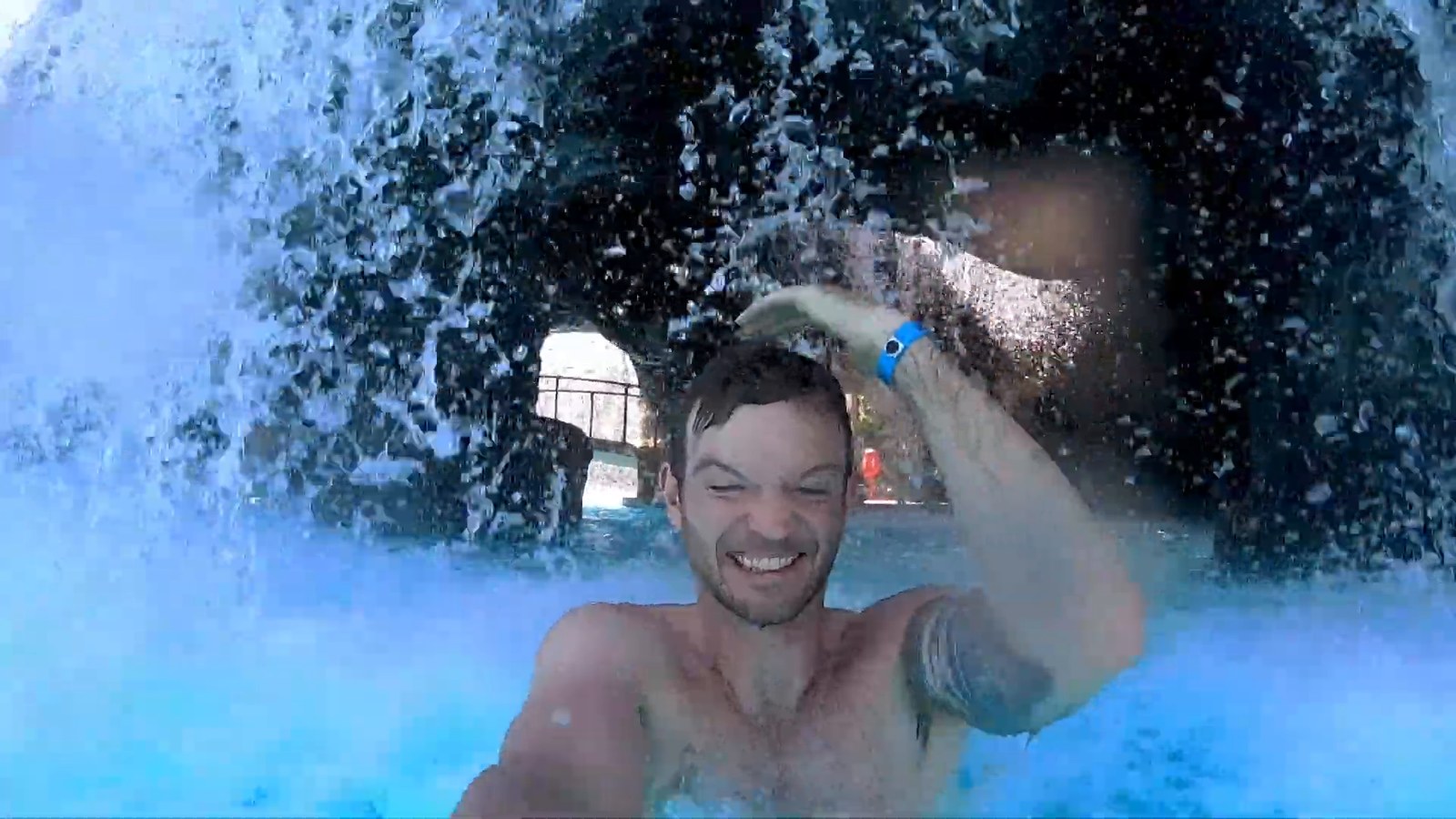 A man grinning as he swims under a waterfall in the cave area of the big pool at Hilton Waikoloa Village.