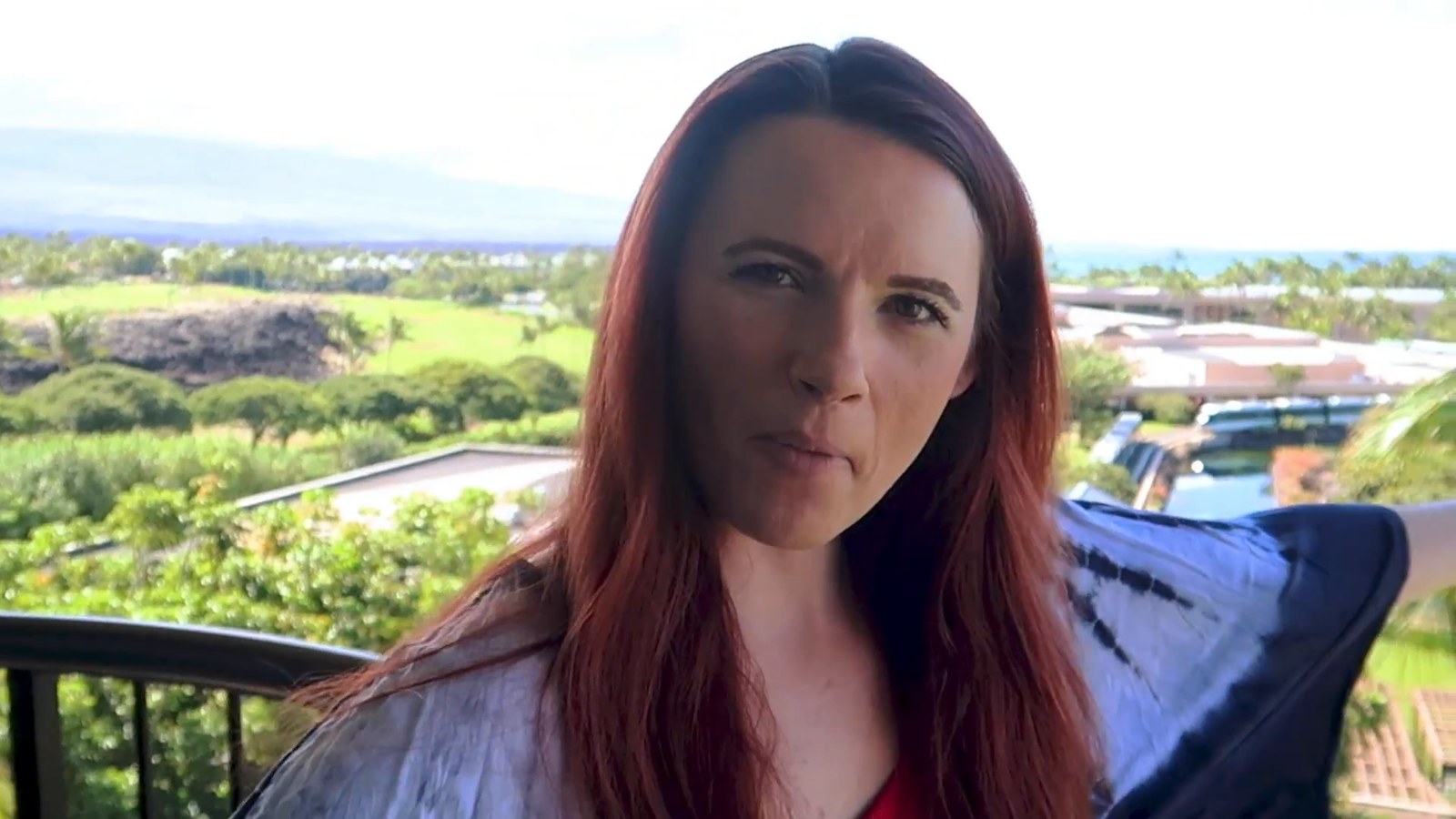A woman on a balcony with a view over green grounds, rooftops and the distant coastline at Hilton Waikoloa Village.