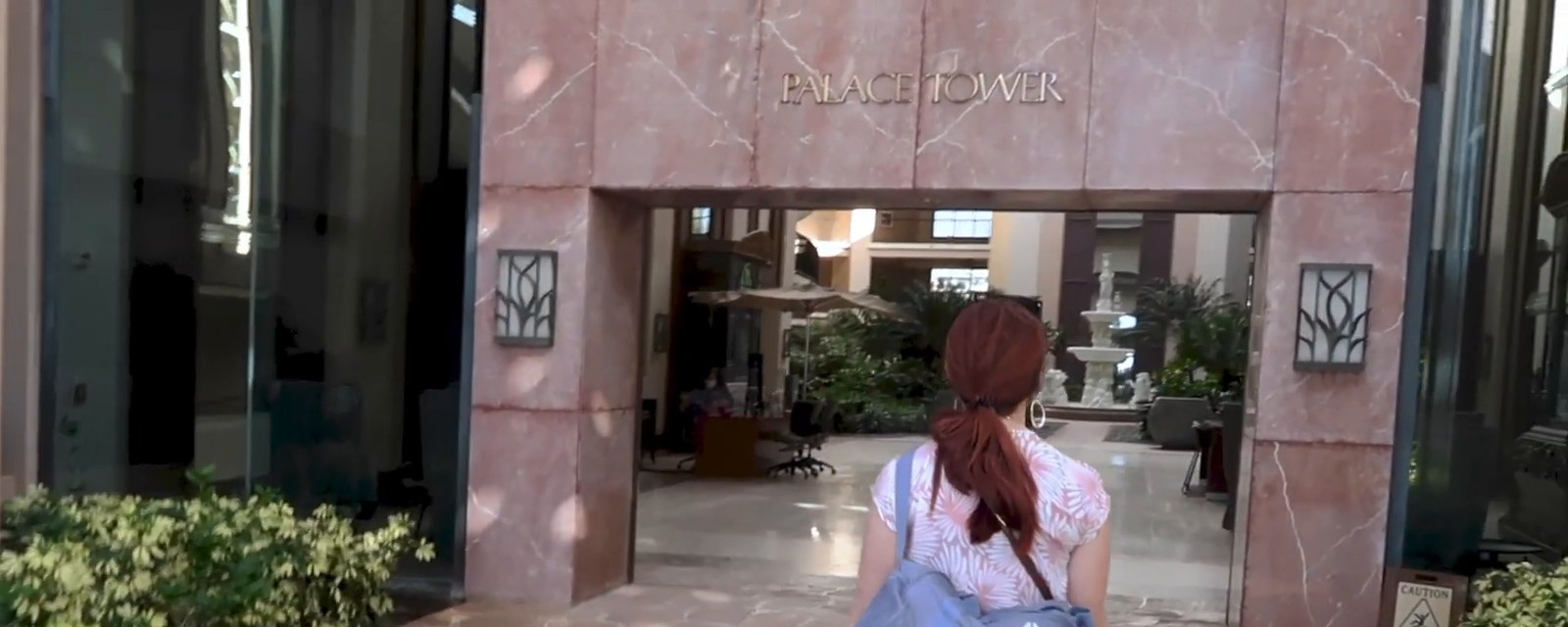 A woman with a duffel bag walking toward the pink marble Palace Tower entrance at Hilton Waikoloa Village.