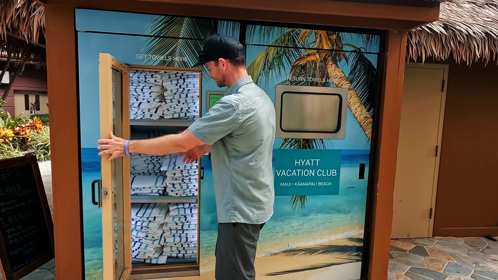 A man opening an automated pool towel cabinet decorated with a beach mural and Hyatt Vacation Club sign.