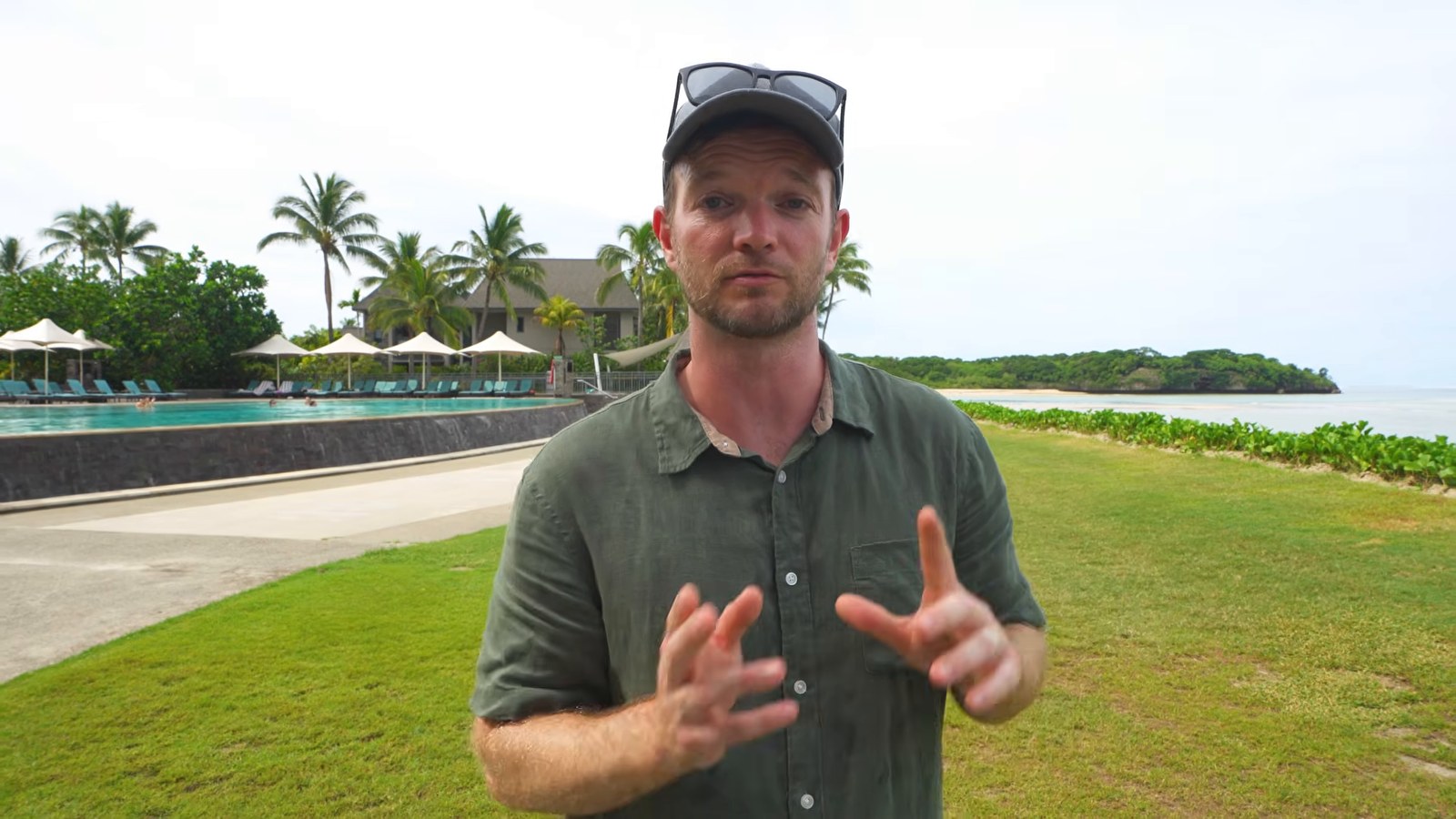 A man standing on the lawn beside the adults-only infinity pool, with loungers, palm trees and the beach behind him.