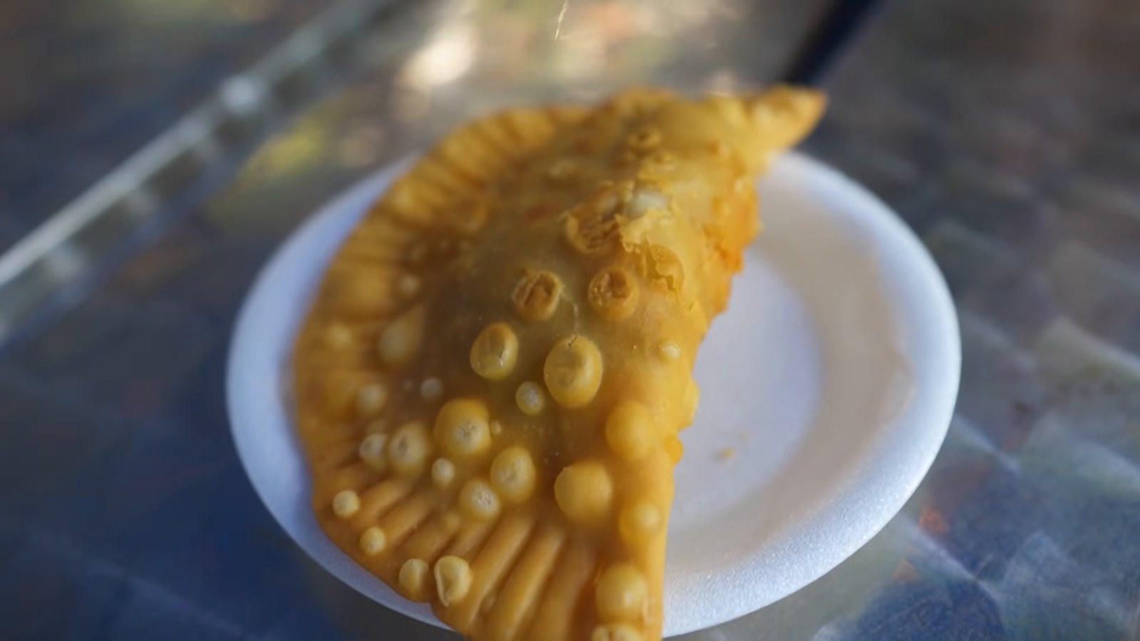 A golden fried empanada on a small white plate on a table.