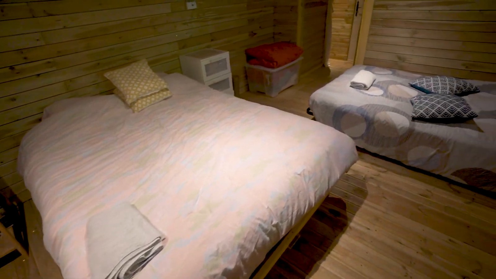 A bedroom with wood-paneled walls, a large bed with a pale duvet and a smaller bed with patterned pillows.