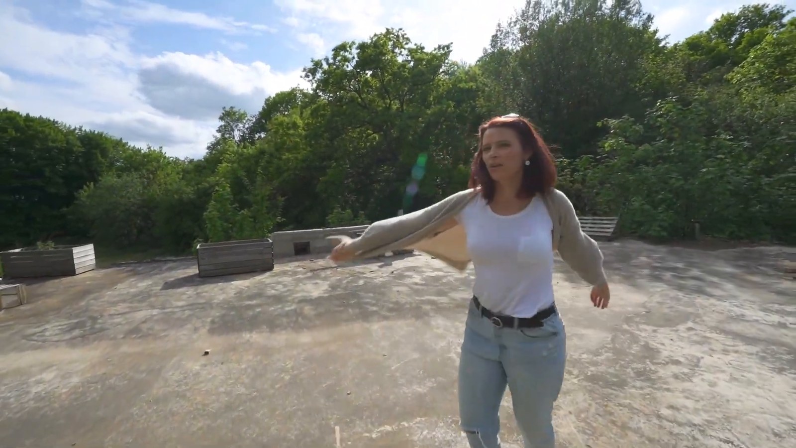 A woman walks across a wide flat concrete roof surrounded by trees under a cloudy sky.