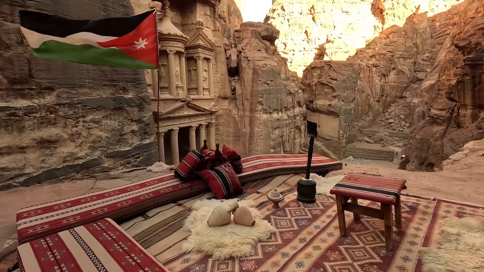 A Jordanian flag, striped cushions, a low stool and rugs set out on a ledge above the Treasury at Petra.