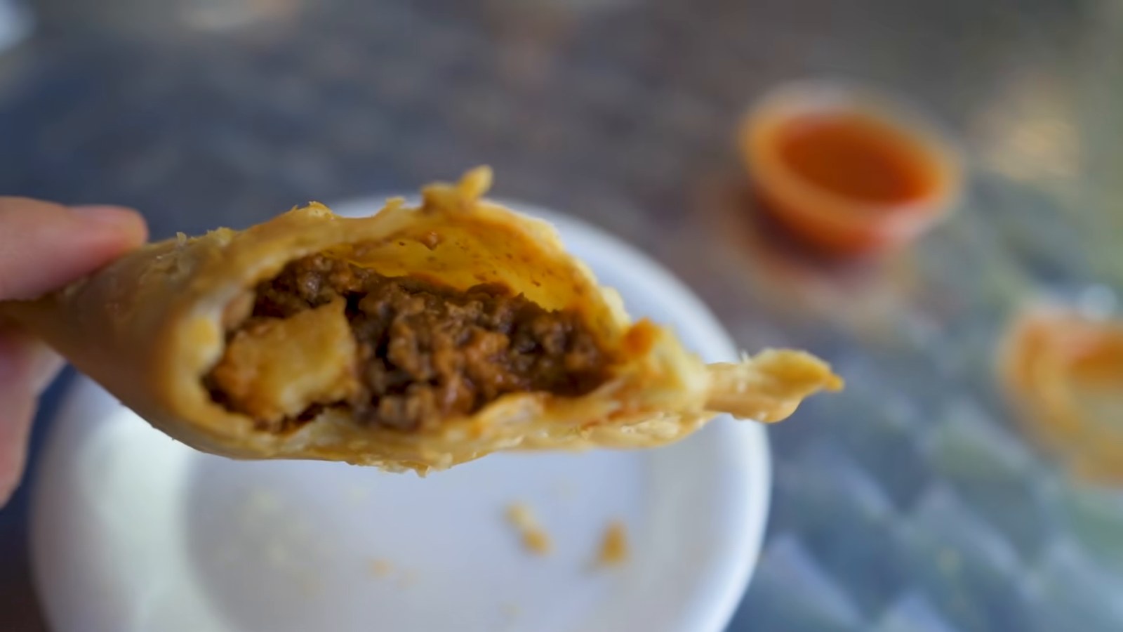 A hand holds a fried empanada broken open to show a filling of ground meat and potato.