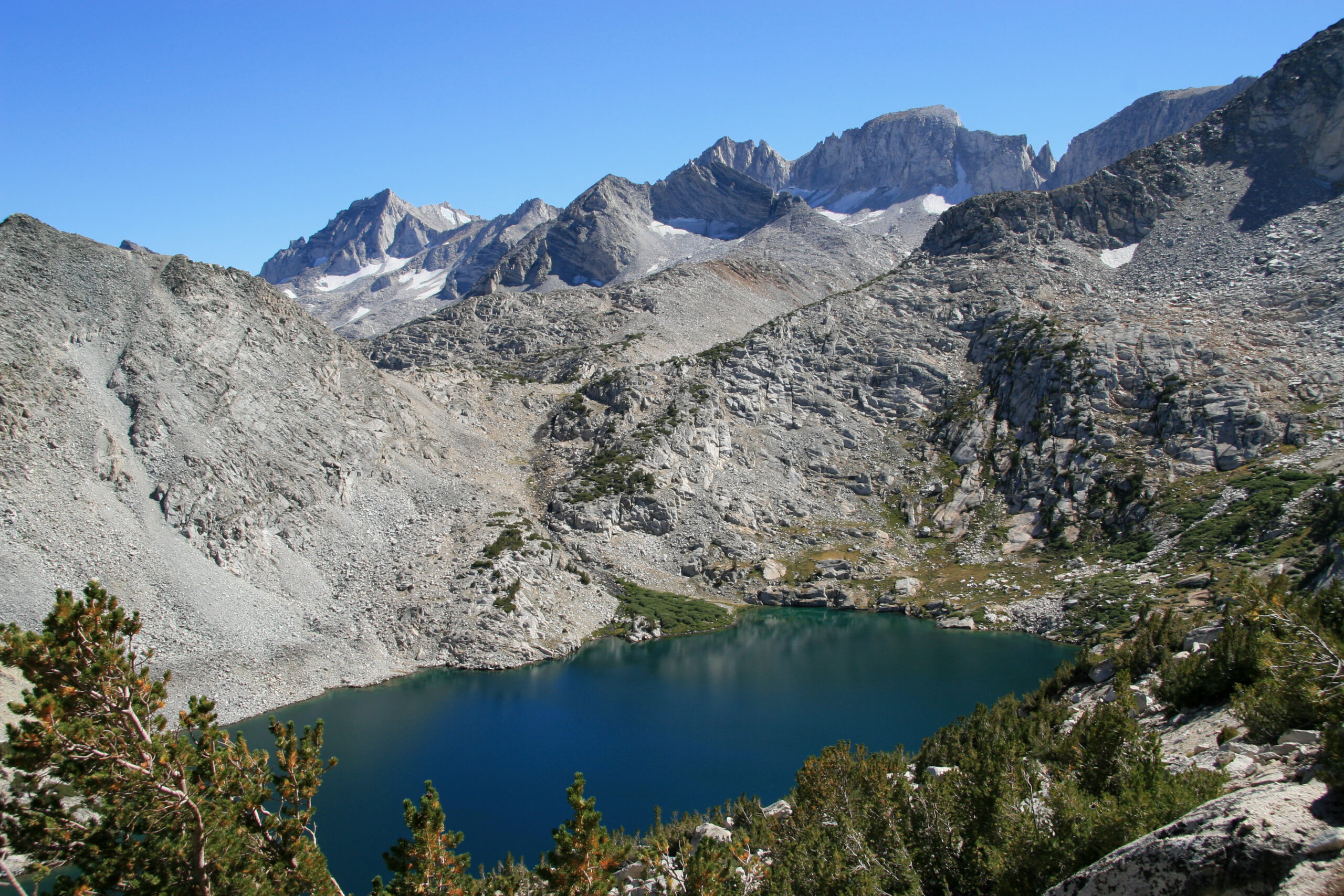 Ruby Lake, a deep blue alpine lake ringed by pale granite slopes and jagged peaks, seen from the trail toward Mono Pass.