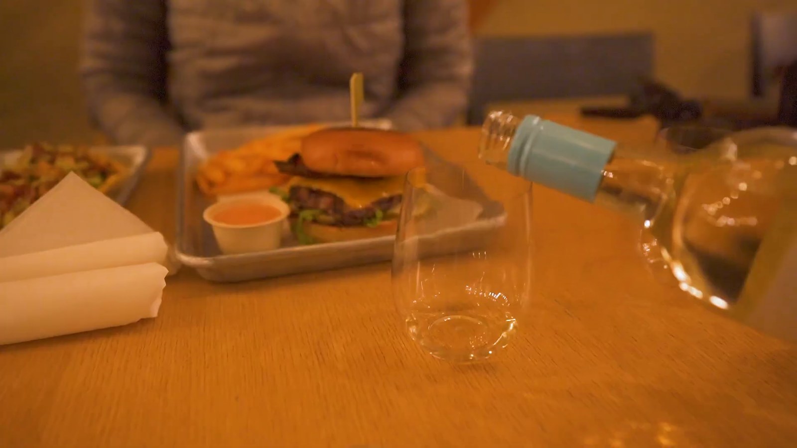 A burger and fries in a metal tray on a wooden table, with a wine glass beside it.