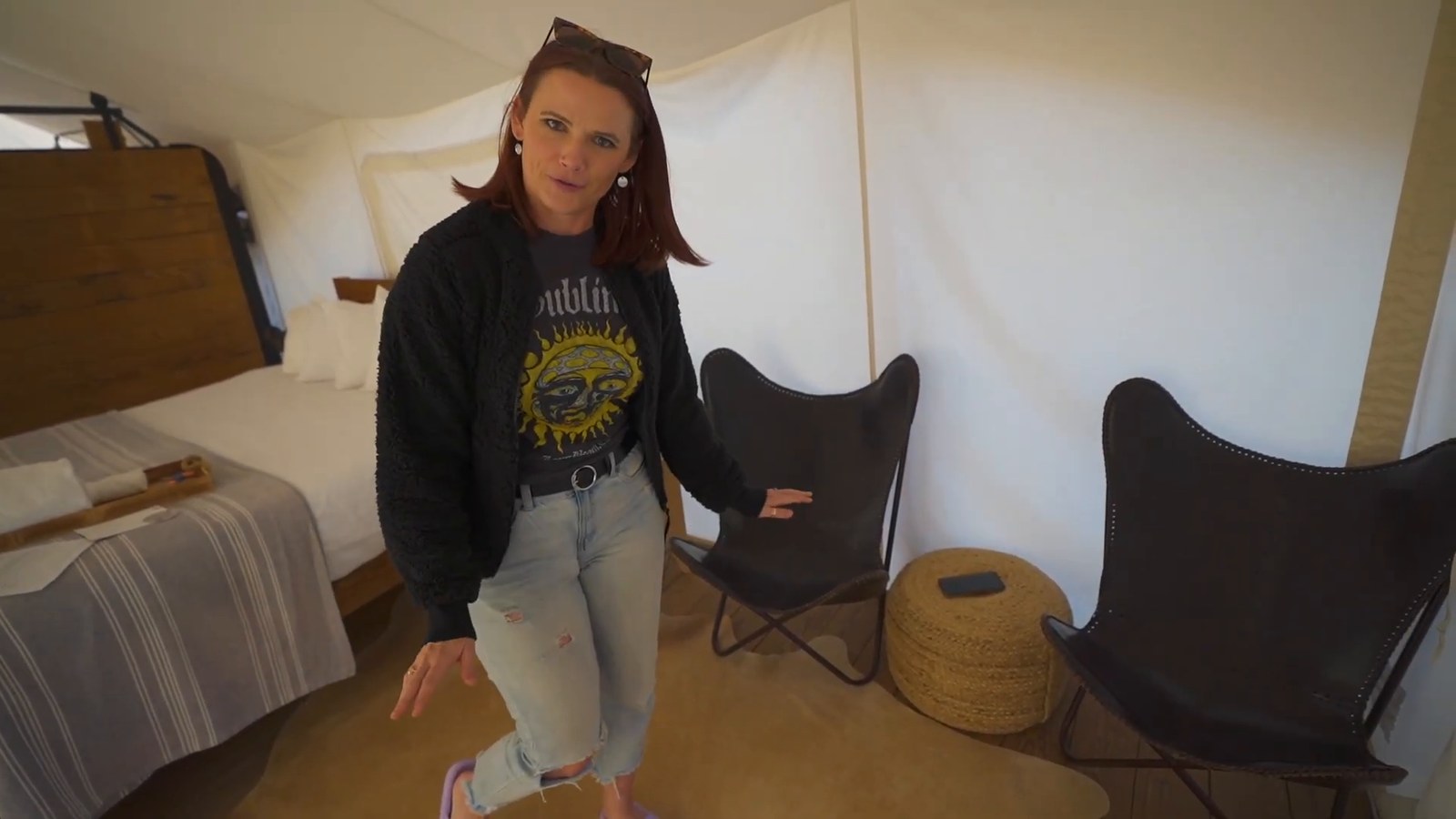 Two black leather butterfly chairs and a woven pouf beside the bed inside the tent.